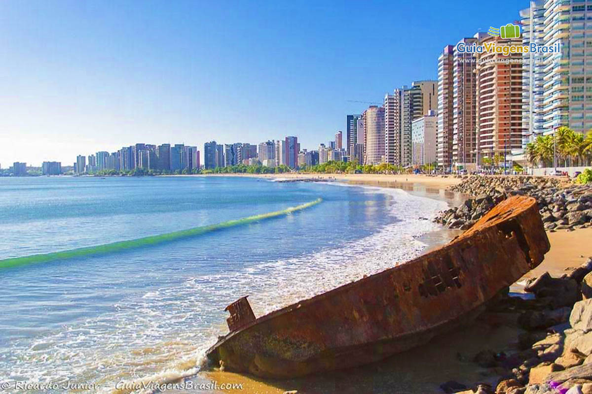 Imagem de um barco enferrujado  sobre as pedras da Praia do Centro em Fortaleza.