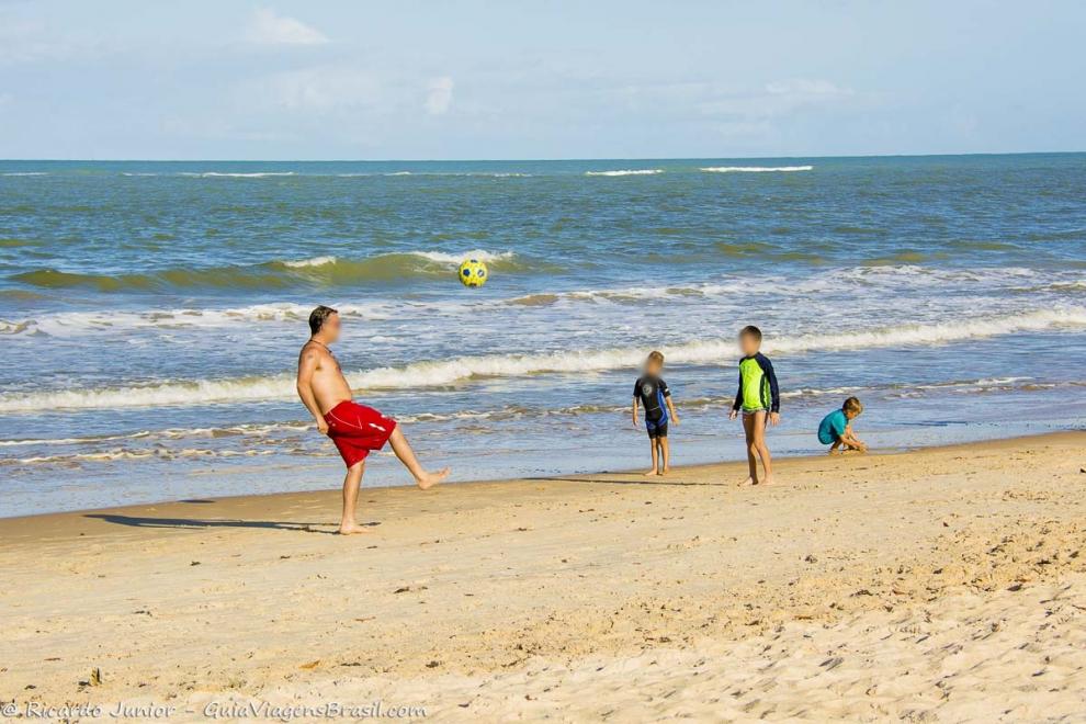 Imagem de crianças jogando bola na beira da praia.