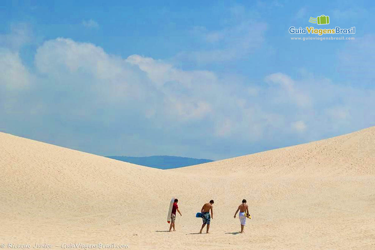 Imagem de amigos com as pranchas subindo as dunas.