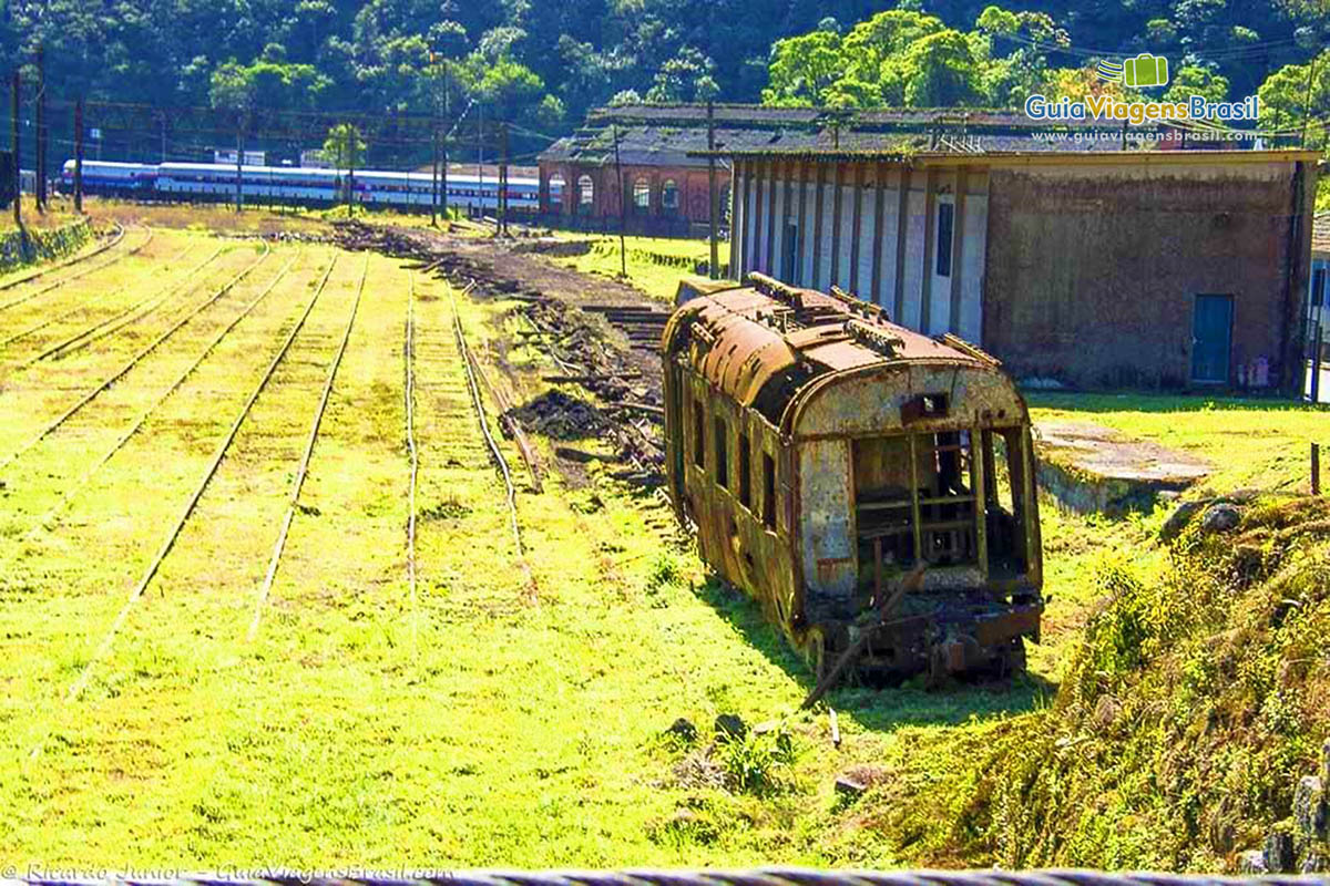 Imagem de um antigo trem de ferro enferrujado, na grama ao lado dos trilhos.