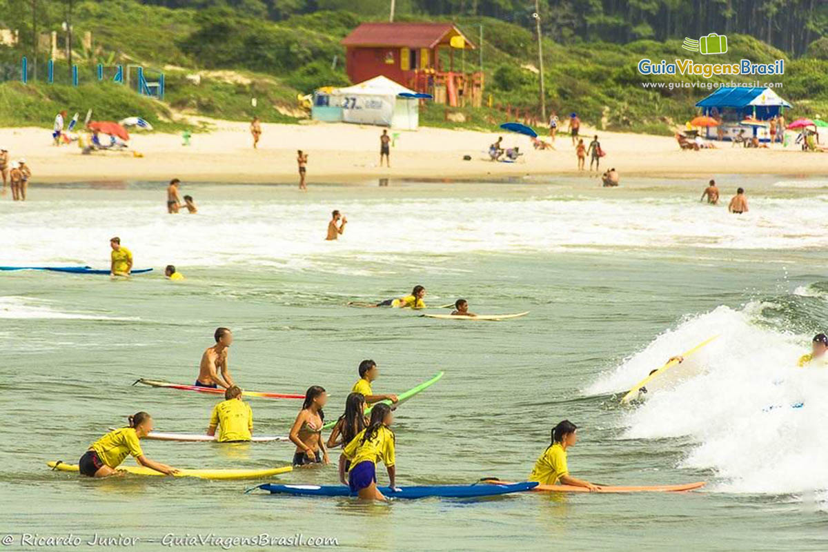 Imagem de pessoas tendo aula de surf no mar da Praia Barra da Lagoa.