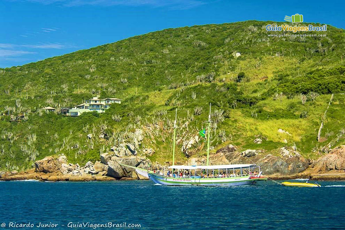 Imagem do barco de passeio se aproximando da ilha e uma bela casa no alto da Ilha.