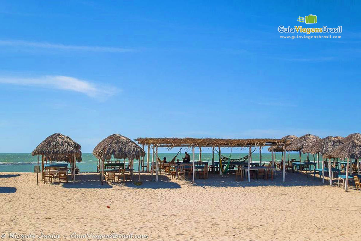 Imagem de barraca de sapê com rede e mesas para turistas, na Praia Macapá.