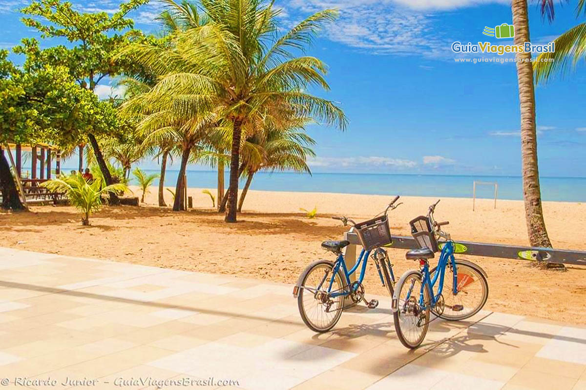 Imagem de duas bicicletas estacionadas no calçadão da praia. 