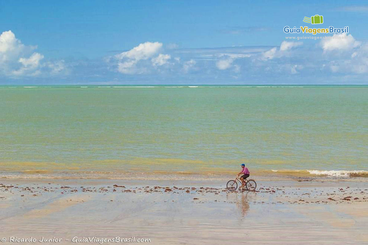 Imagem de uma pessoa andando de bicicleta na beira da praia.