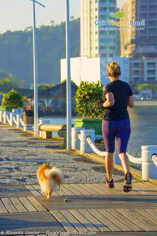 Imagem de uma moça e seu cachorrinho correndo na orla da praia em Camboriú.