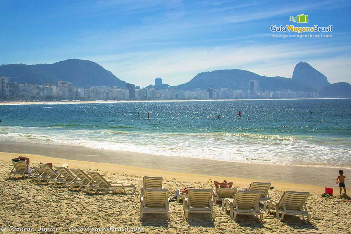 Imagem de cadeiras brancas para deitar nas areias da praia.