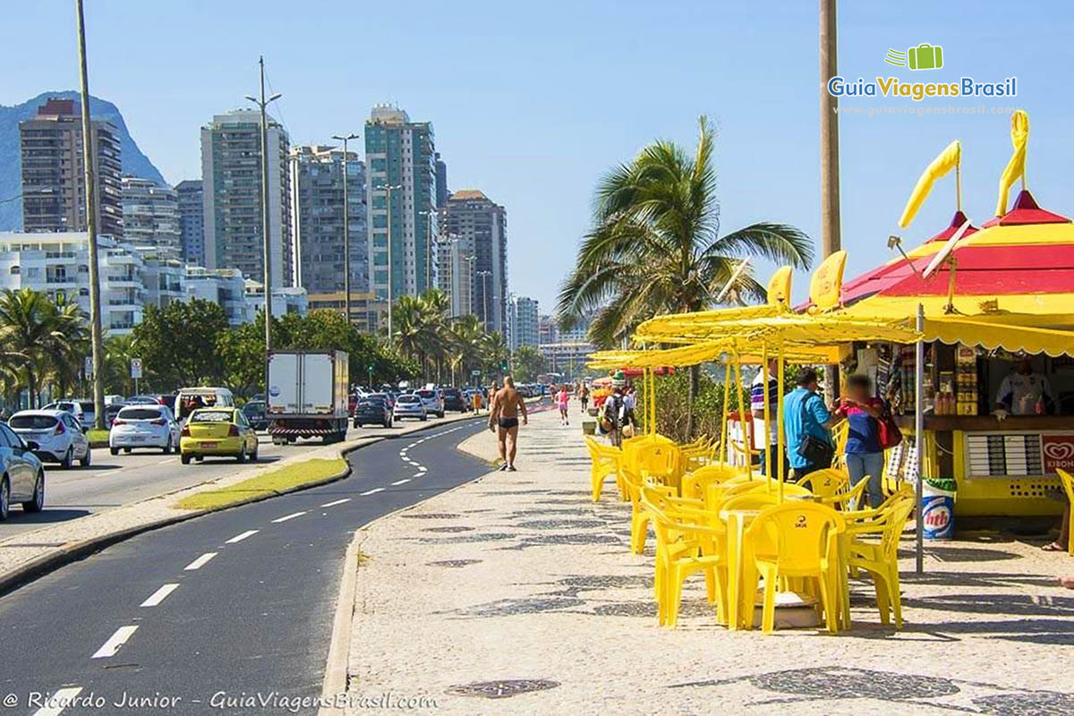 Imagem da bela orla com prédios na av., ciclovia e calçadão com quiosques, na Praia Barra Tijuca.