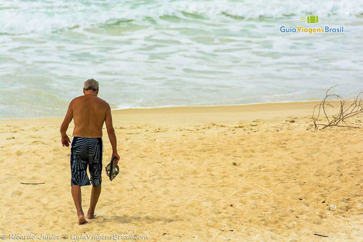 Imagem de um senhor caminhado pelas areias da praia.