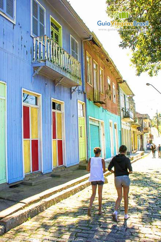 Imagem de moradoras andando pelas ruas e casa de madeira pintada de azul.