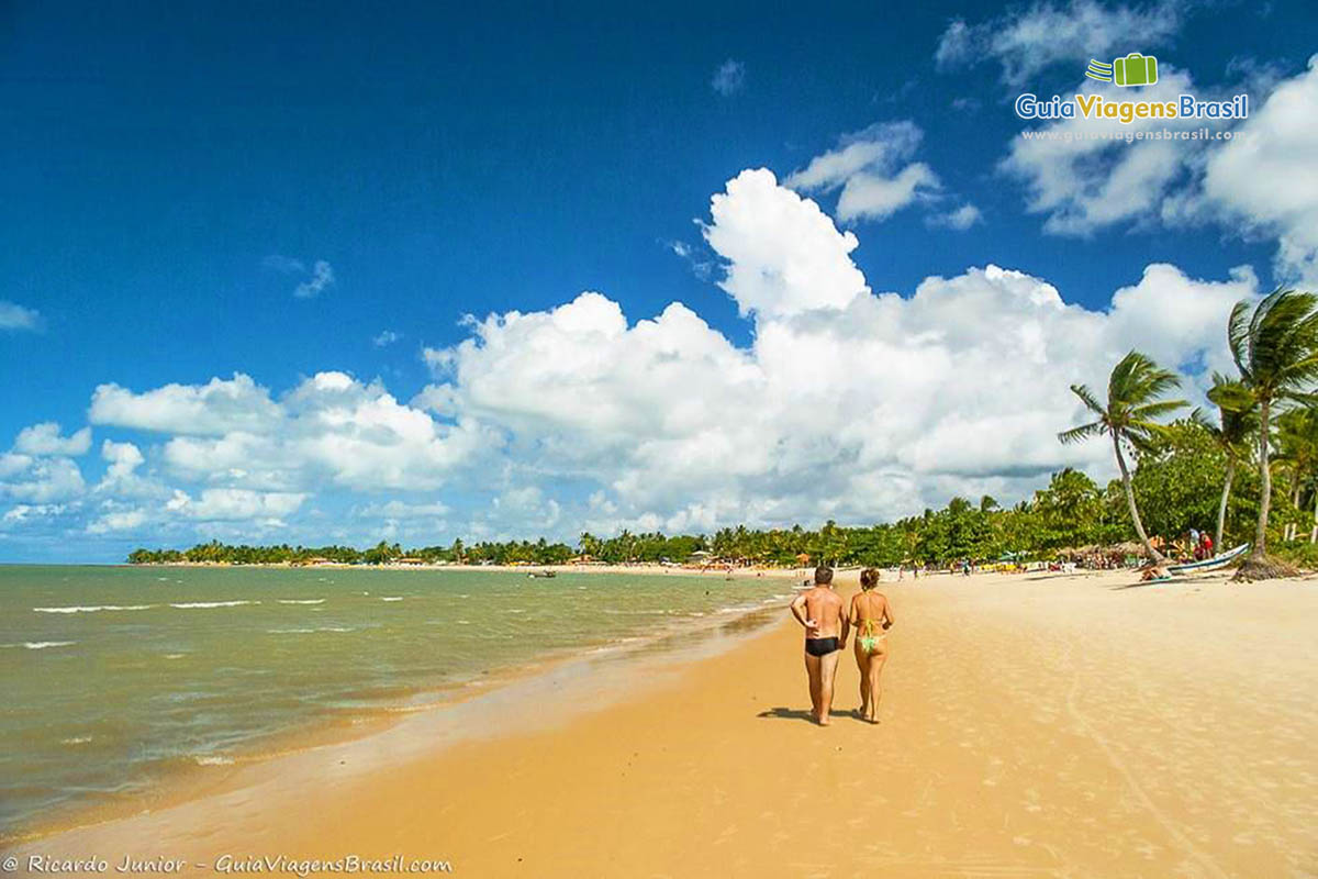 Imagem de casal andando nas areias da belíssima praia.