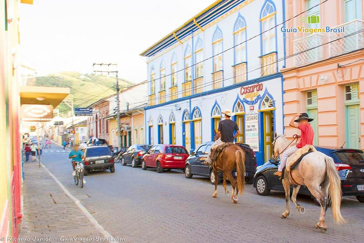 Imagem de pessoas andando de cavalo pelas ruas da cidade.