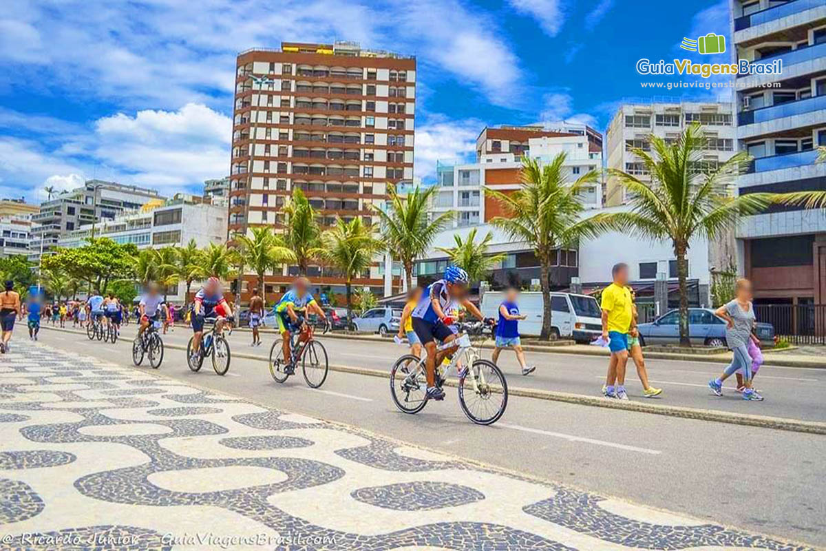 Imagem de vários ciclistas passando pela orla da Praia do Leblon.