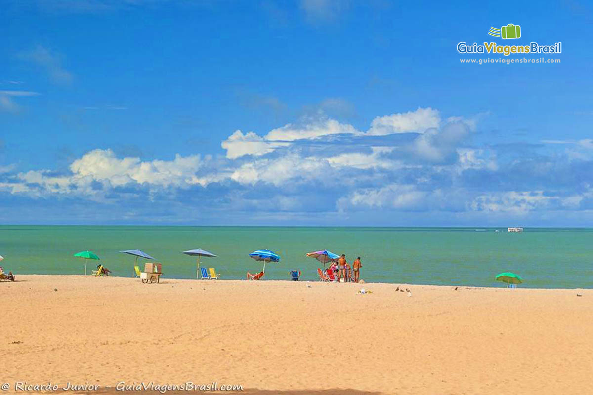 Imagem de vários guarda sol coloridos na areia e o mar encantador da Praia Tambaú, João Pessoa.