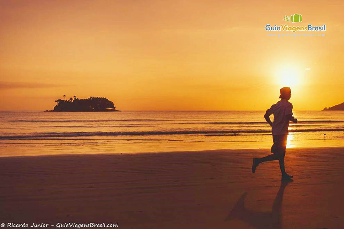 Imagem de uma pessoas correndo na beira da praia e ao fundo um lindo por do sol.