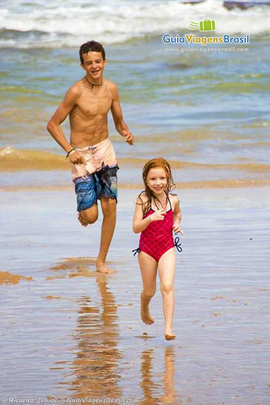 Imagem de crianças brincando de pega pega na beira da praia.
