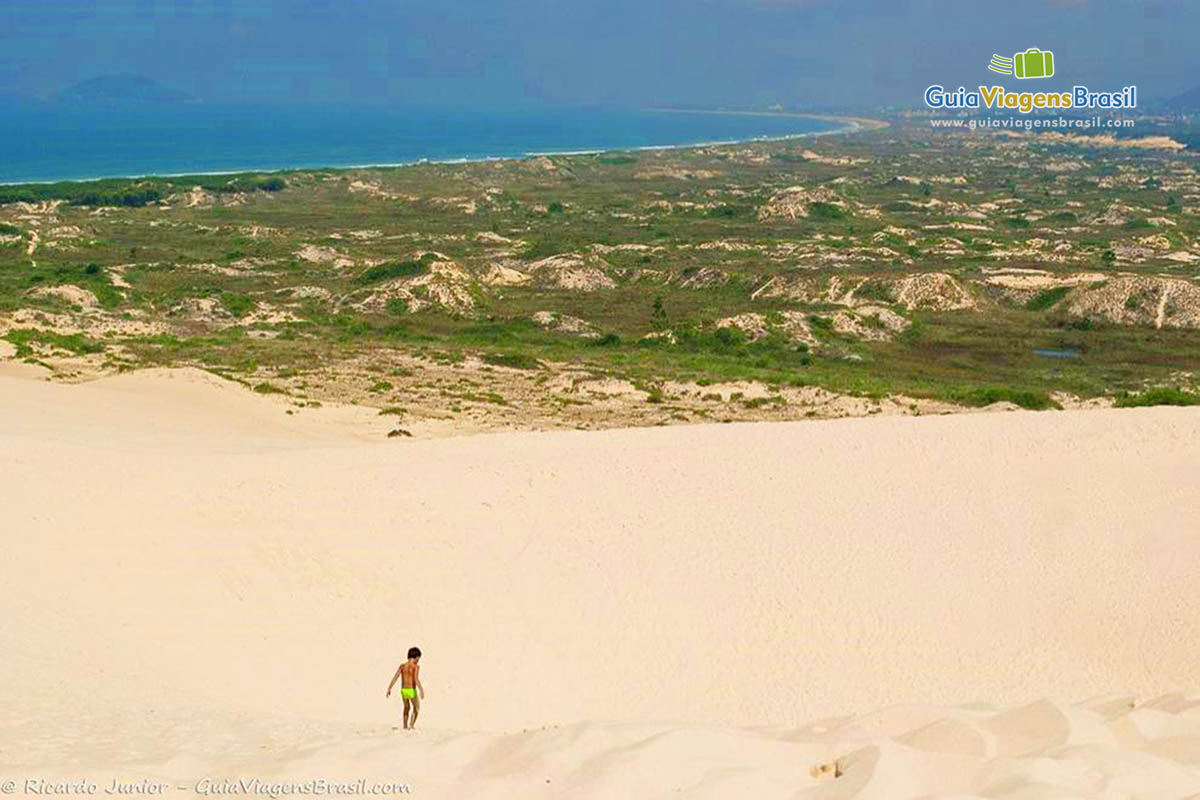 Imagem de uma criança no alto das dunas e no horizonte a bela paisagem da Lagoa.