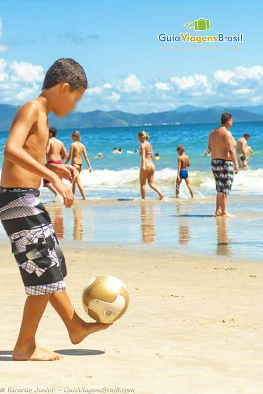 Imagem de um menino fazendo embaixada na areia da praia.