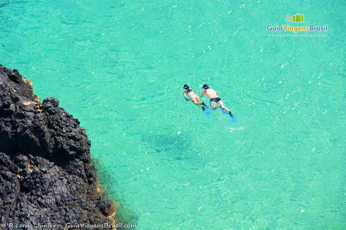Imagem de dois turistas mergulhando nas águas cristalinas da Baía dos Porcos, em Fernando de Noronha, Pernambuco, Brasil.