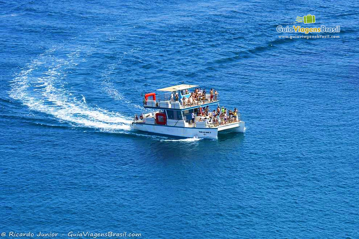 imagem de um barco com turistas navegando nas águas azuis da Baía dos Porcos em Fernando de Noronha, Pernambuco, Brasil.