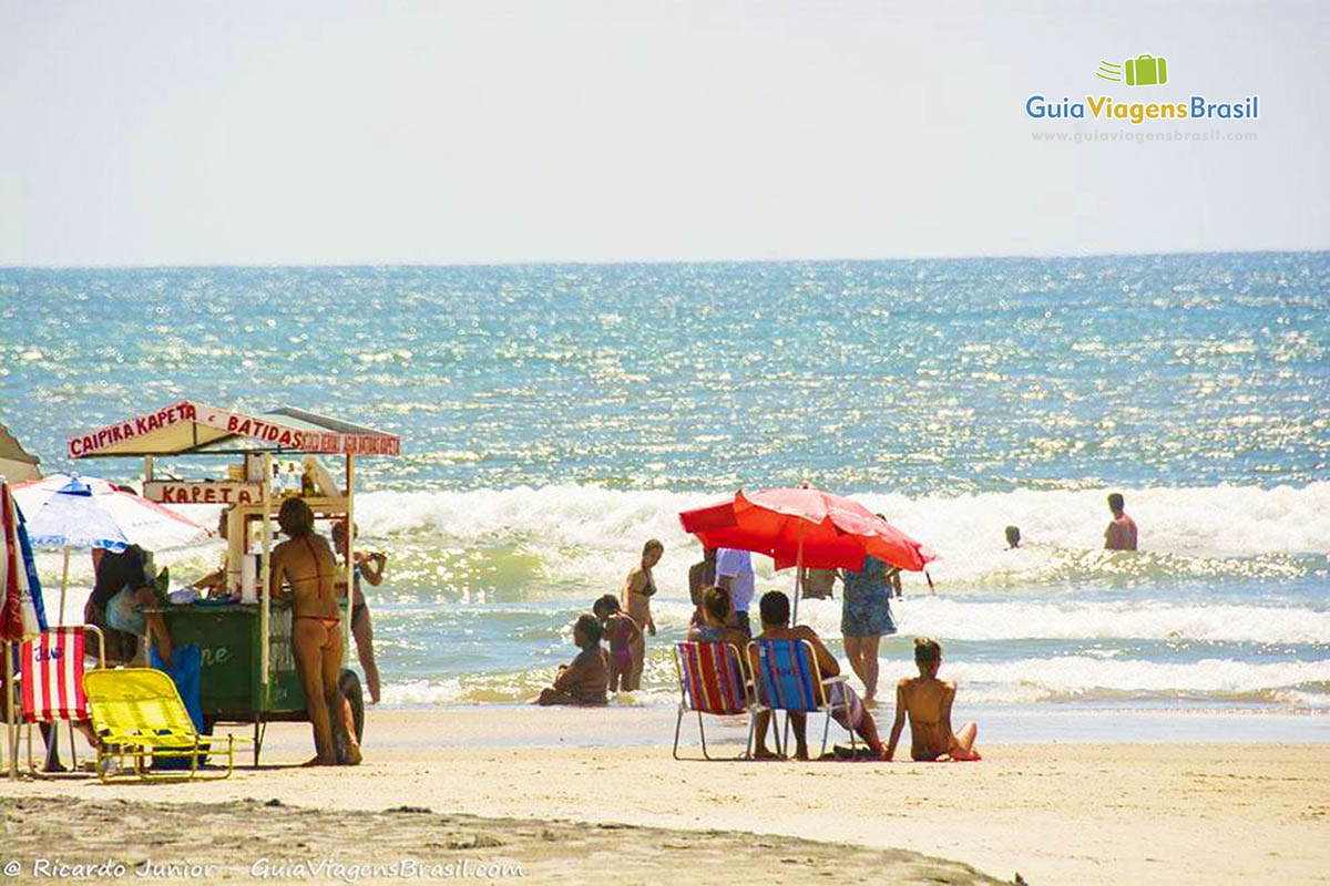 Imagem da Praia Brava, com carrinho de bebidas e turistas na areia da praia, em Caiobá, Santa Catarina, Brasil.