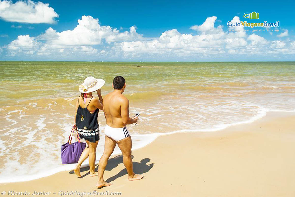 Imagem de casal caminhando na beira do mar dessa maravilhosa praia.