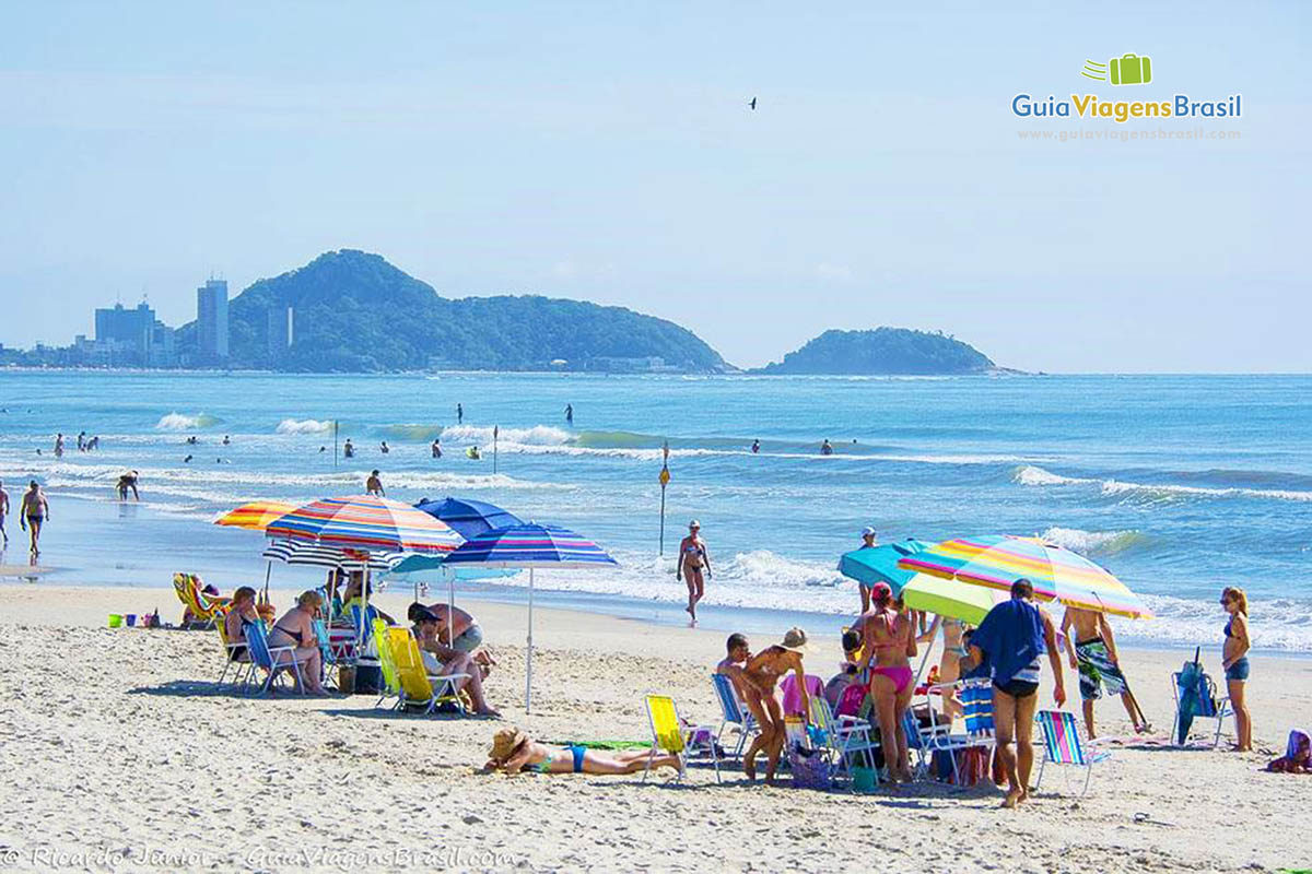 Imagem de guarda-sol coloridos e turistas curtindo uma tarde agradável na Praia Central de Guaratuba, em Santa Catarina, Brasil.