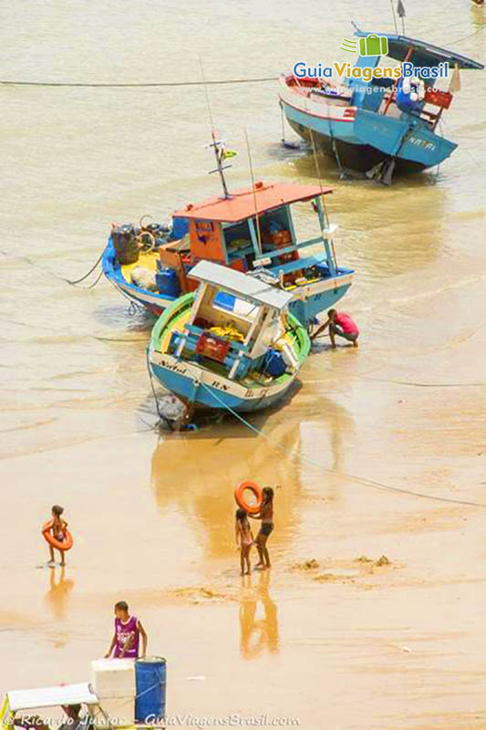 Imagem de crianças próximo a barco de pescadores na areia.