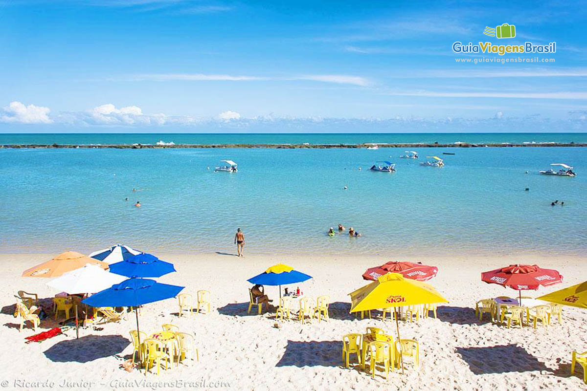 Imagem da Praia Barra de São Miguel, com guarda sol espalhados na areia, em Alagoas, Brasil.