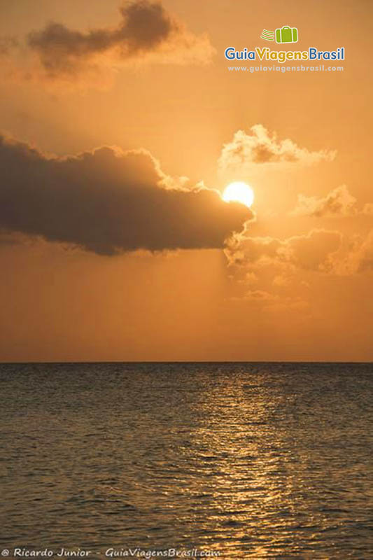 Imagem do pôr do sol, na cor alaranjado, no horizonte sob o mar. Paisagem inesquecível, na Praia da Conceição, em Fernando de Noronha, Pernambuco, Brasil. 
