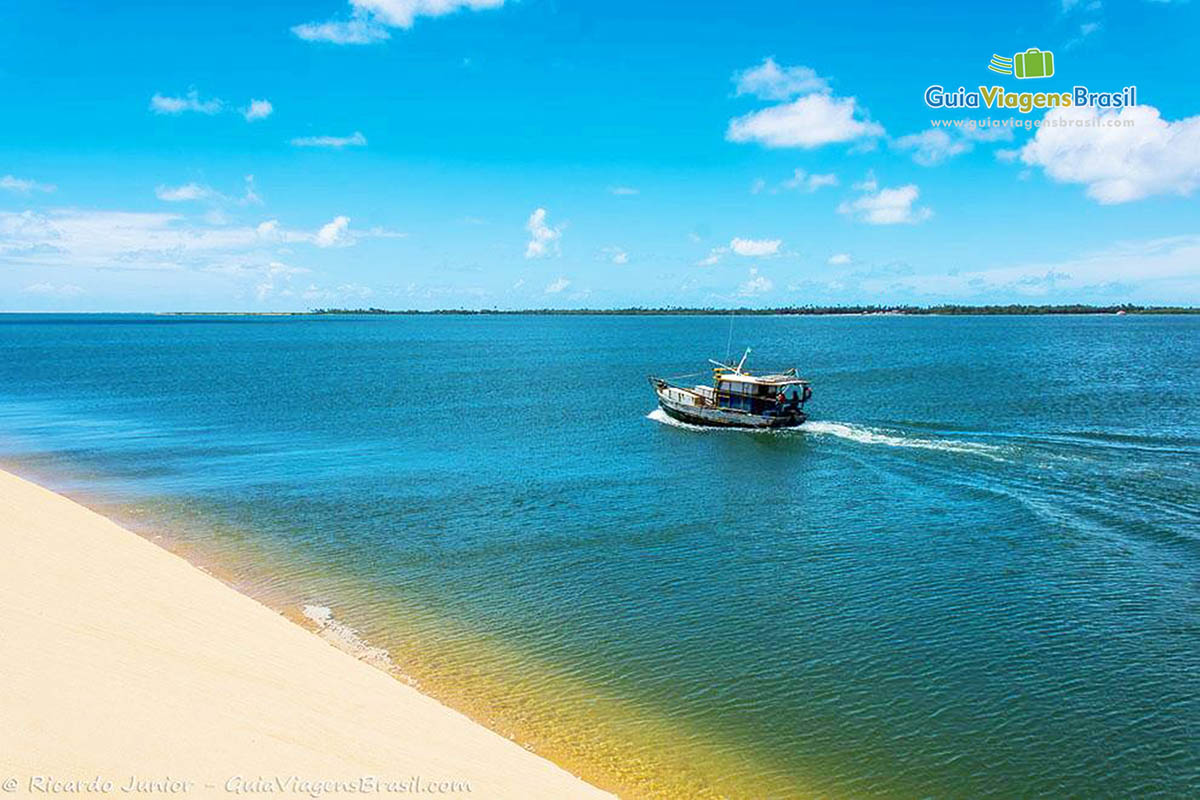 Imagem visto alto das dunas, onde tem visão de uma barco navegando nas águas belas de Foz Rio São Francisco, em Alagoas, Brasil.