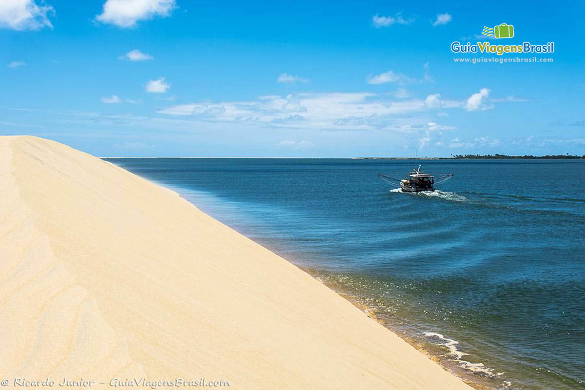 Imagem das dunas e nas águas claras uma barco passeando, em Alagoas, Brasil.