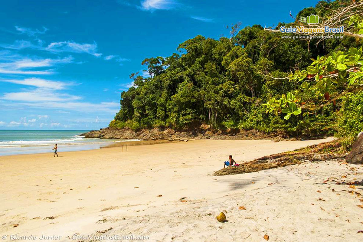 Imagem de menino sentado na pedra da praia admirando o mar.