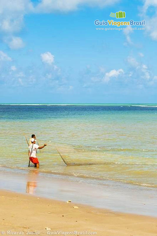 Imagem de pescadores jogando a rede nas águas da Praia de Bitingui. 