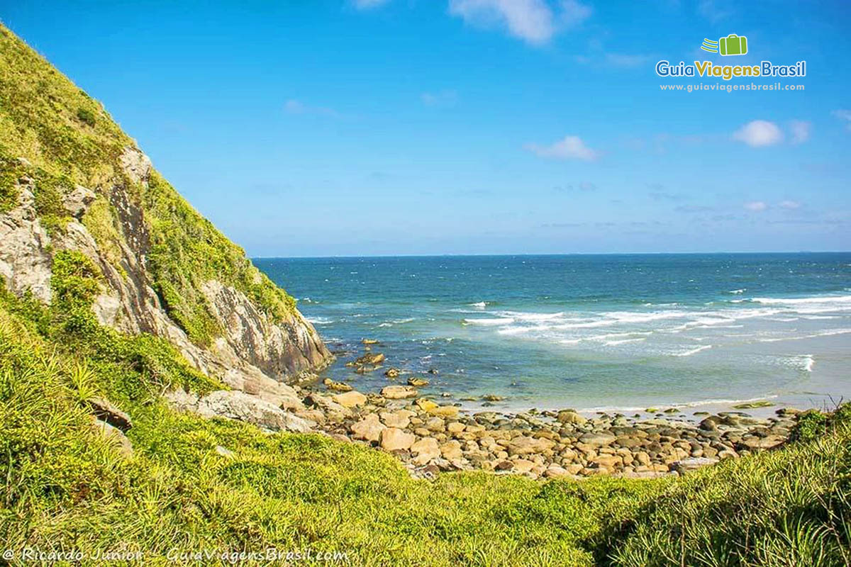 Imagem vista do canto da praia onde tem as pedras e as águas cristalinas, na Praia de Fora, na Ilha do Mel, Paraná, Brasil.