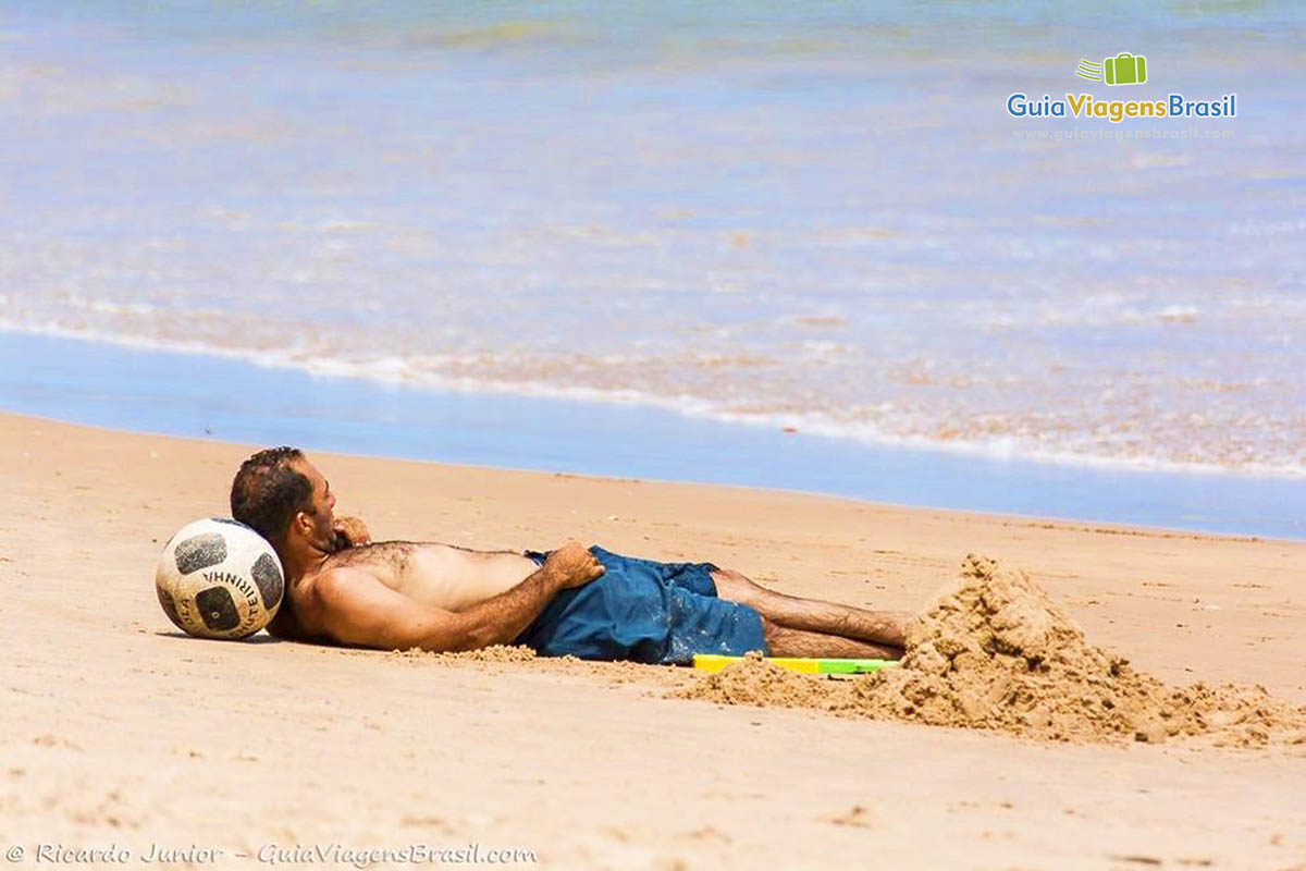 Imagem de um rapaz deitado na areia admirando a bela paisagem.