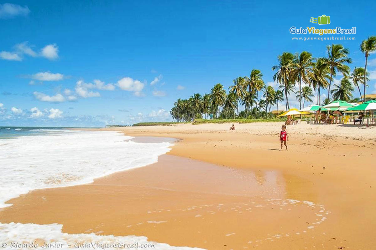 Imagem de uma criança andando nas areias da Praia Guarajuba.