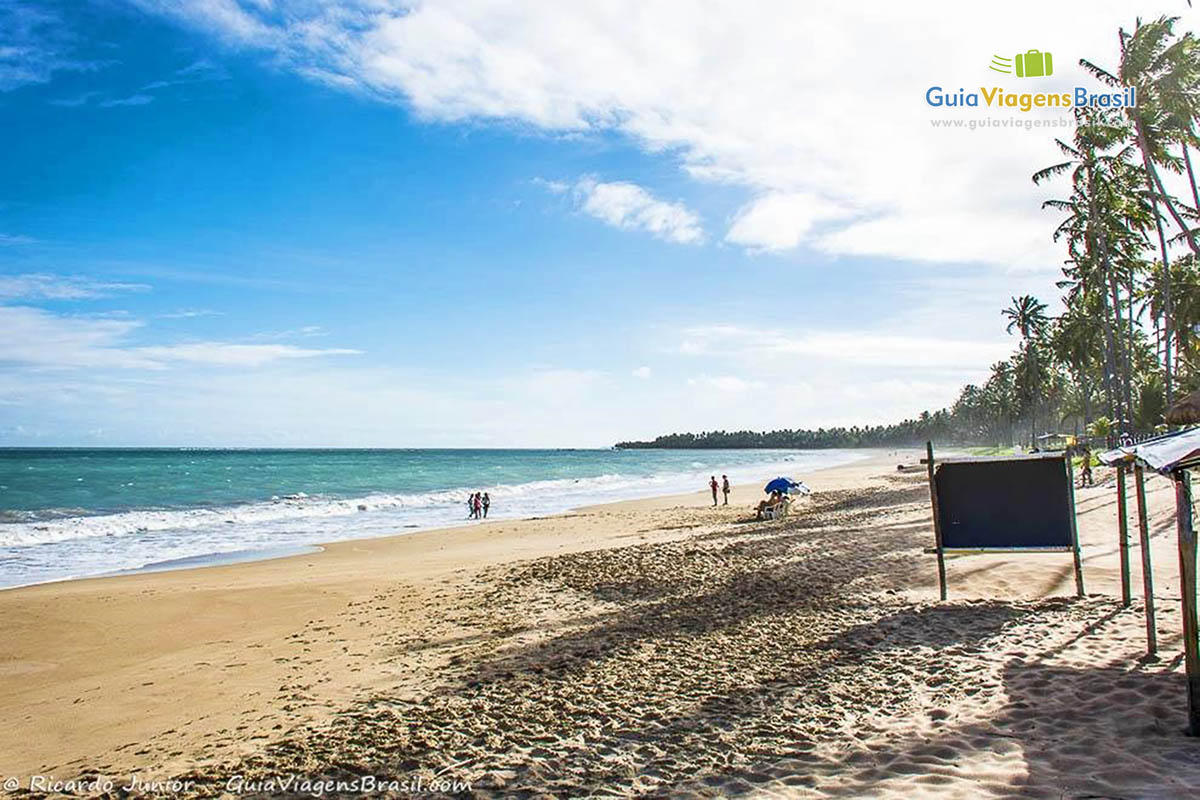 Imagem de toda extensão da praia com turistas caminhando na beira do mar na Praia de Guaxuma, em Maceió, Alagoas, Brasil. 