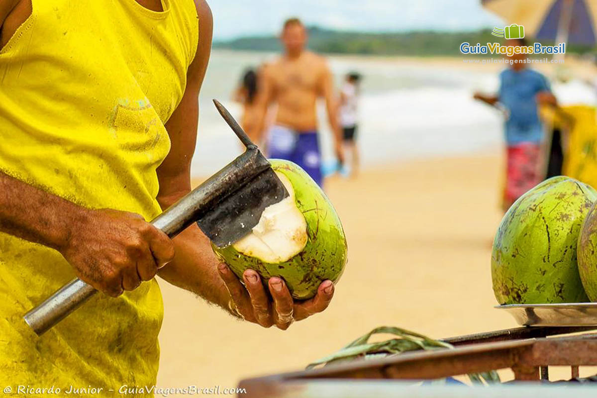 Imagem de vendedor abrindo coco na praia.