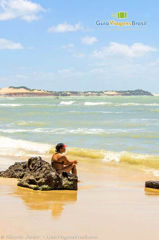 Imagem de uma mulher sentada na pequena rocha e admirando o mar de Pipa.