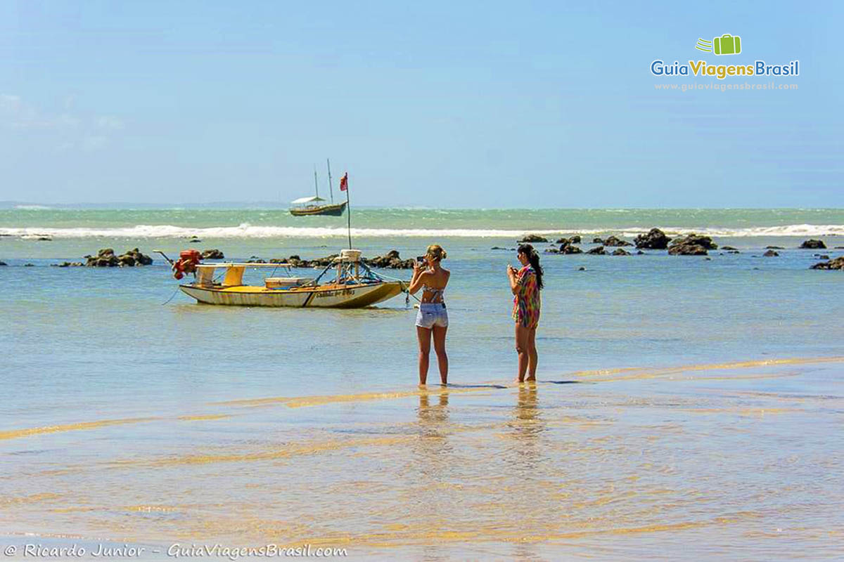Imagem de duas turistas tirando foto dessa paisagem encantadora que é a Praia de Pipa.