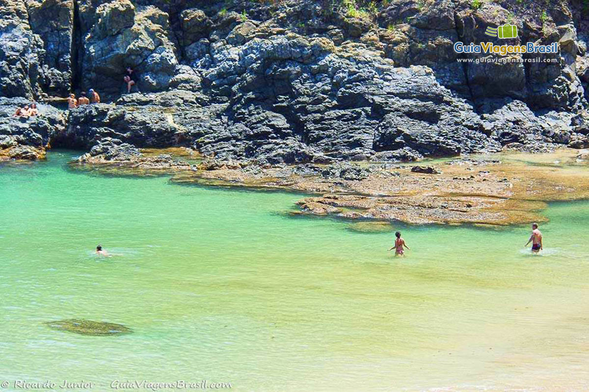 Imagem de turistas explorando não apenas o mar mas as pedras da Praia do Cachorro, em Fernando de Noronha, Pernambuco, Brasil.