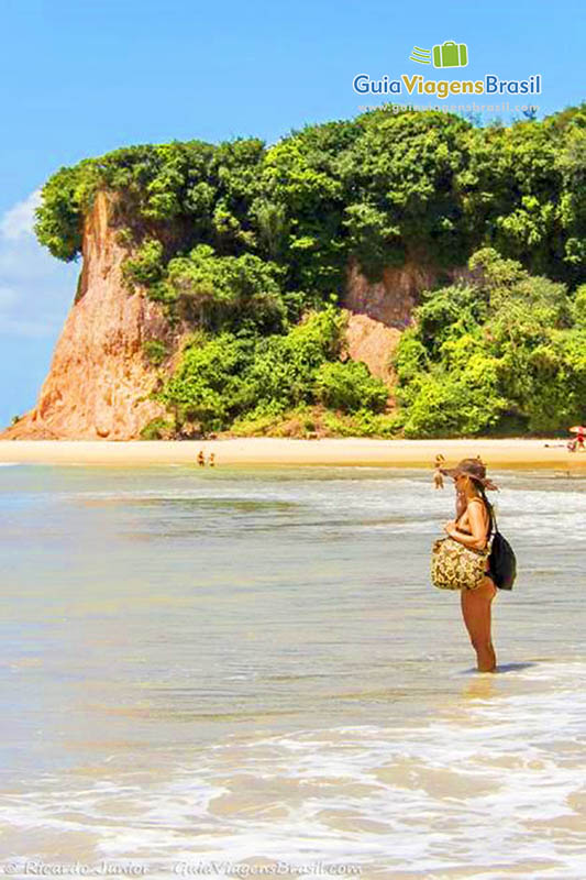 Imagem de uma turista com os pés na água admirando a beleza da Praia do Curral.