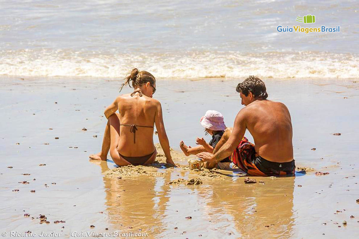 Imagem de família brincando na areia com sua filha.