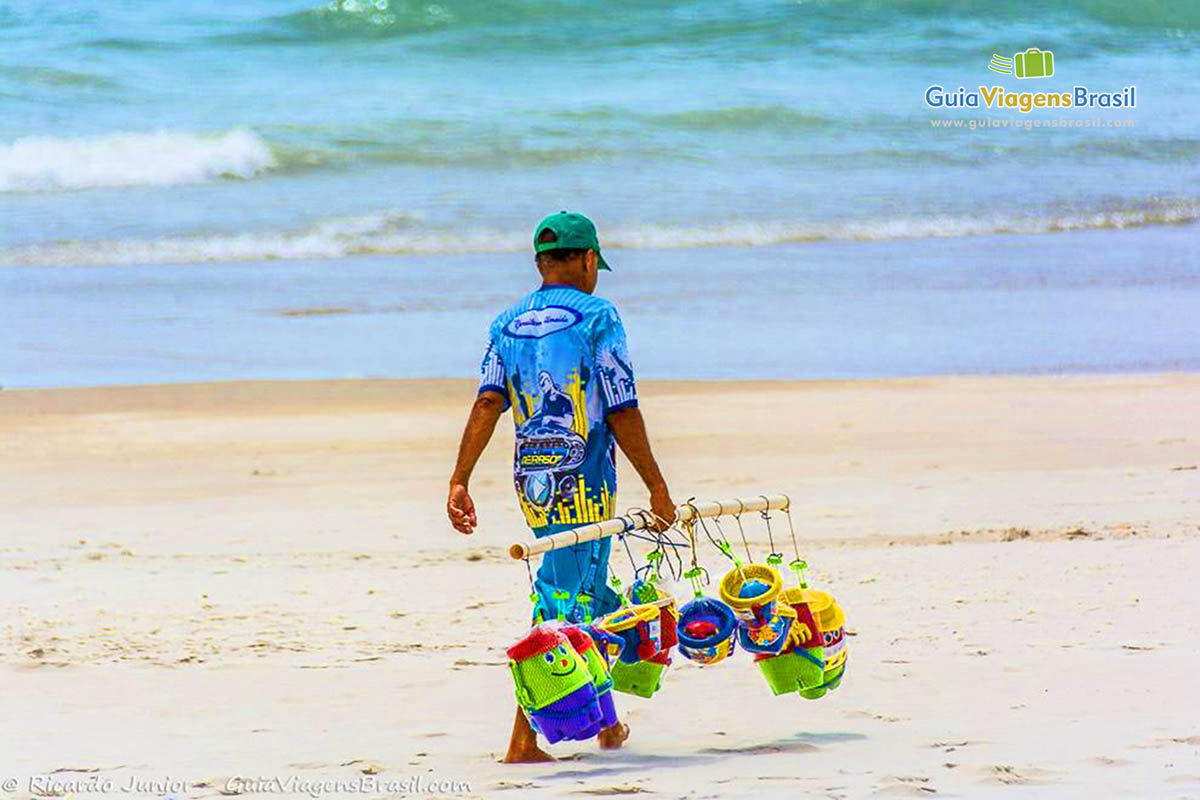 Imagem de vendedor ambulante com baldes de crianças, na Praia do Gunga, em Maceió, Alagoas, Brasil.