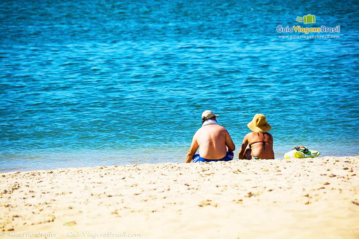Imagem de casal de turistas sentados a beira mar, curtindo a bela paisagem da Praia do Gunga, em Maceió, Alagoas, Brasil.