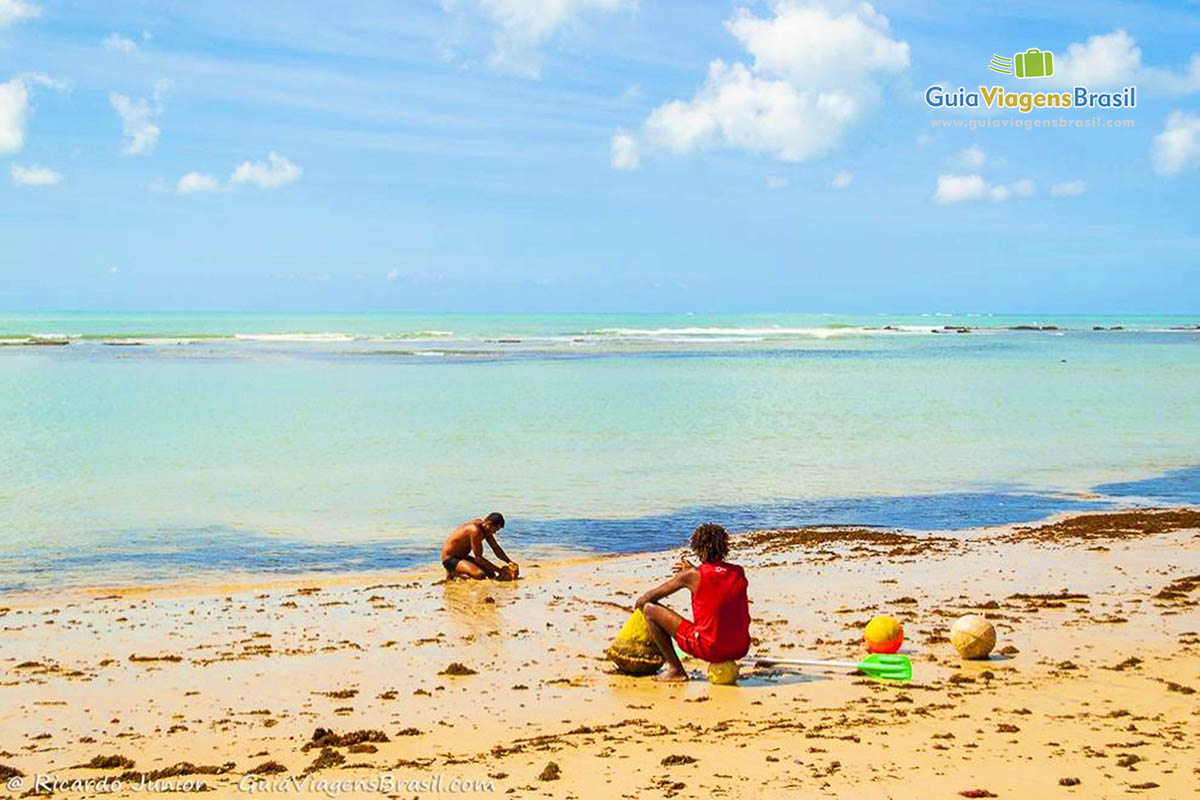Imagem de pessoas sentadas na beira do mar, na Praia do Parracho.