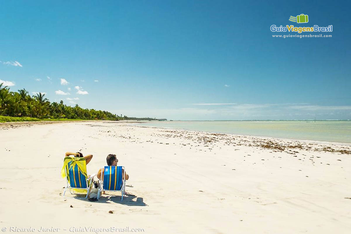 Imagem de casal sentados em cadeira nas areias da Praia do Toque.