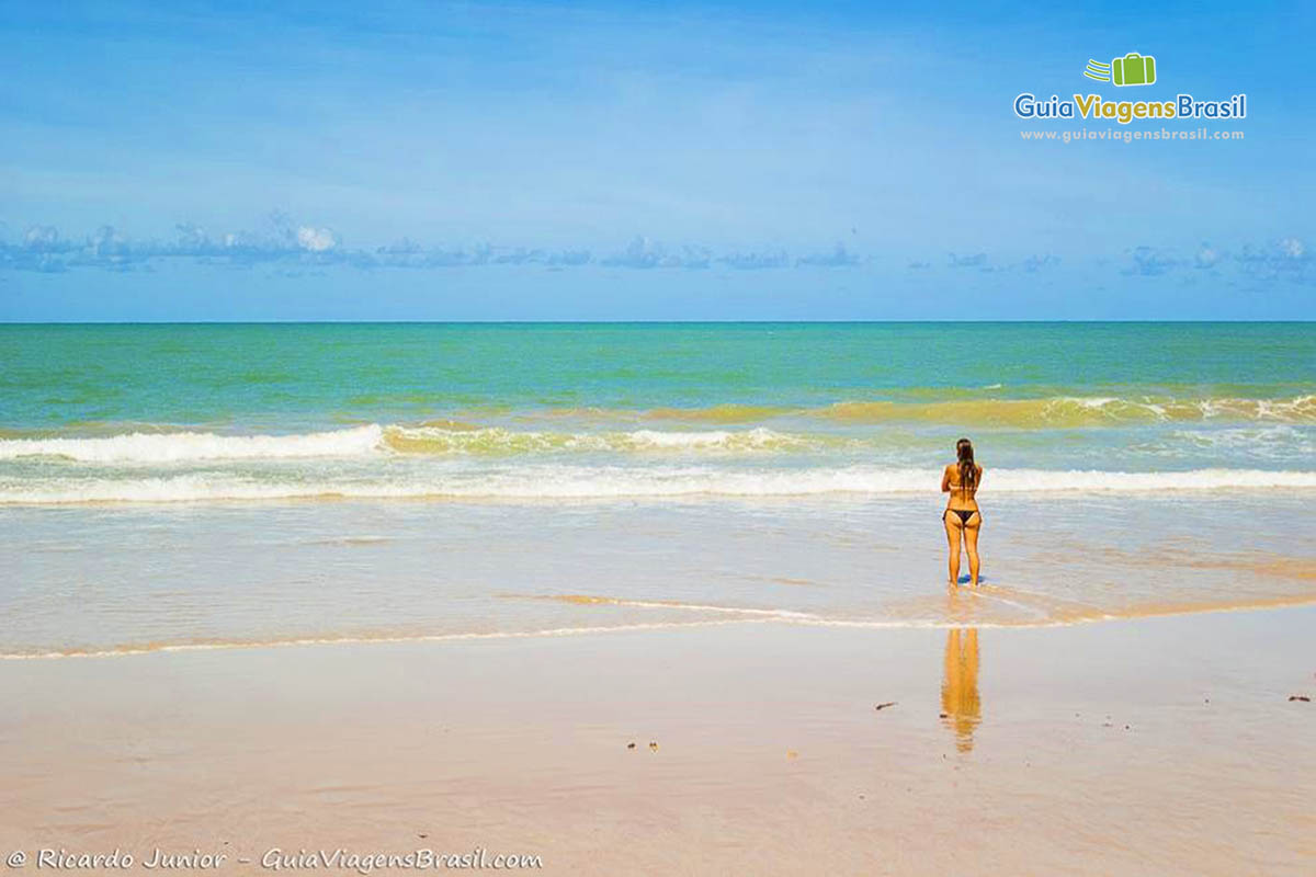Imagem de turista na beira da água admirando a cor do mar.
