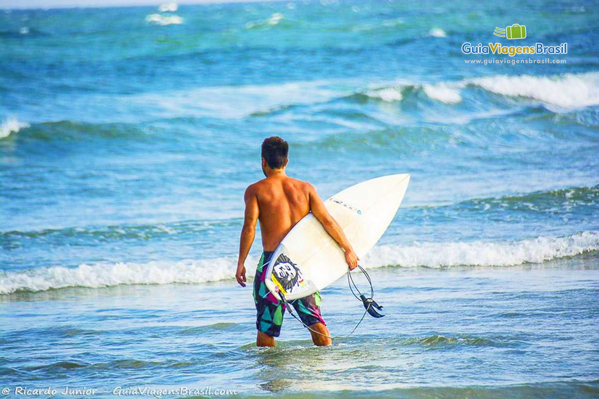 Imagem de surfista entrando nas águas da Praia Grande, na Ilha do Mel, Paraná, Brasil.